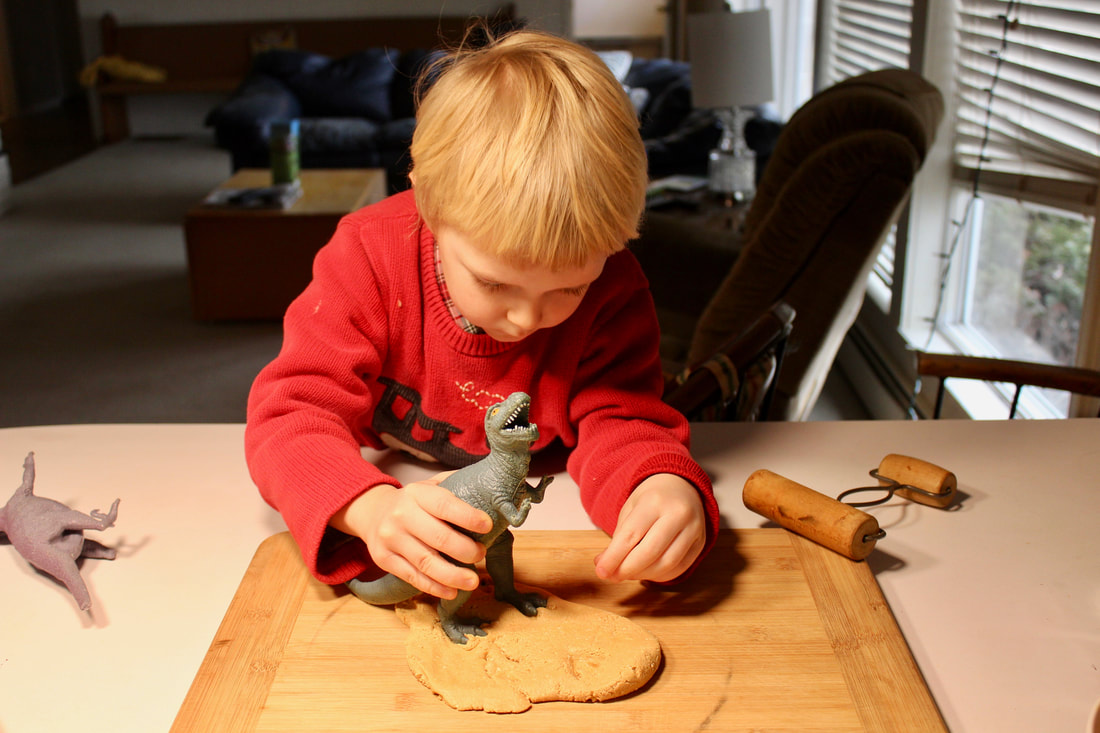 Child making dinosaur prints in peanut butter play dough