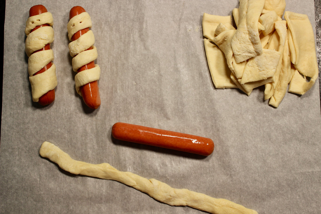 Wrapping strips of dough around hot dogs to make the mummy dogs